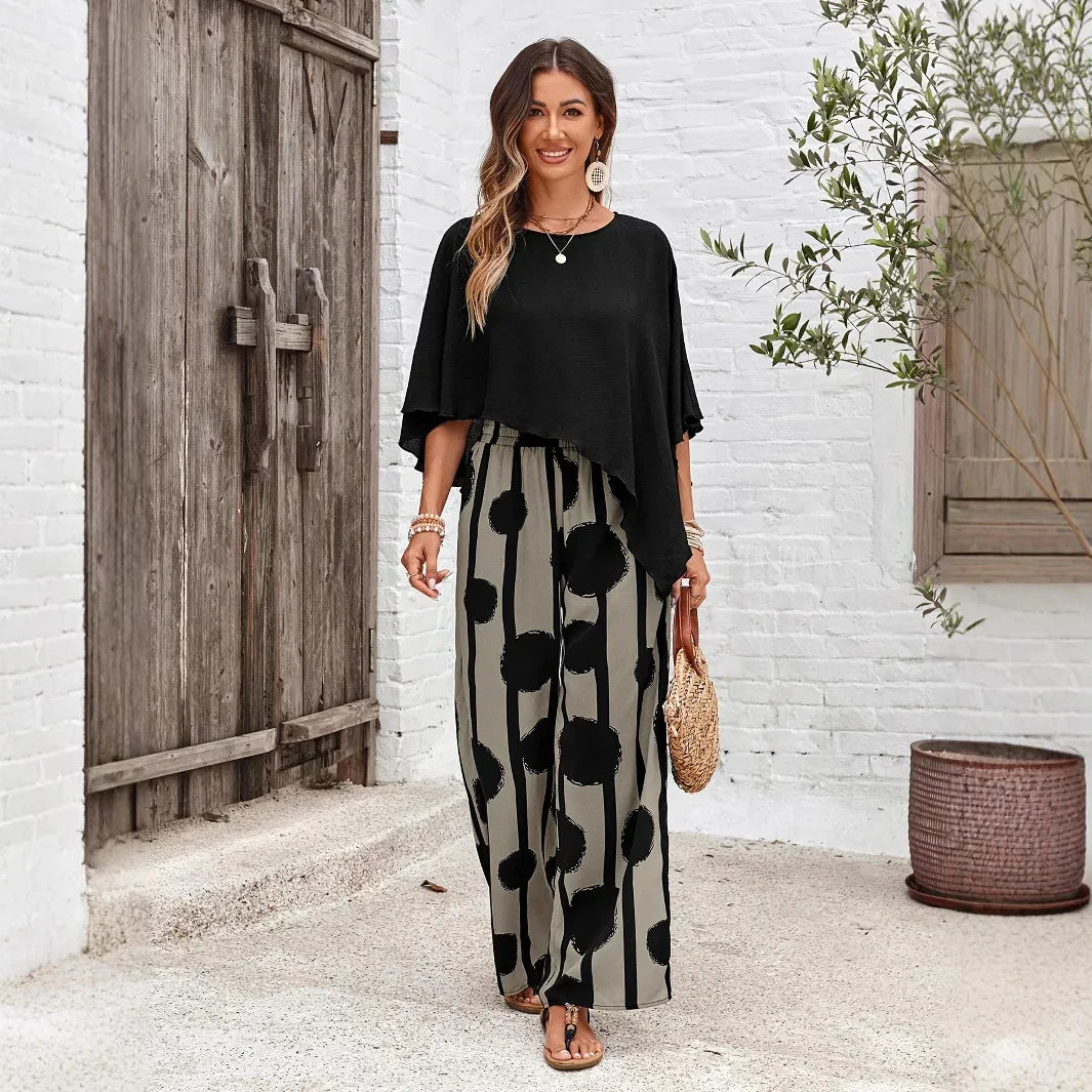 Woman in black asymmetrical top and patterned wide-leg pants walking by rustic wooden door and white brick wall