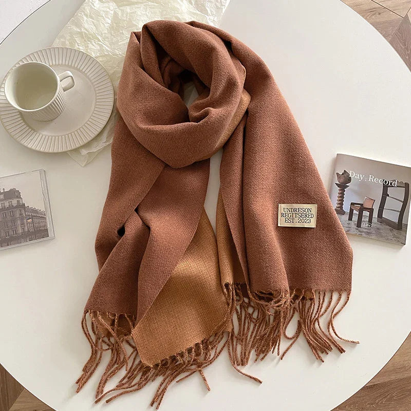 Brown wool scarf with fringe and label on white table with cup and books