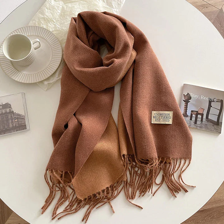 Brown wool scarf with fringe and label on white table with cup and books