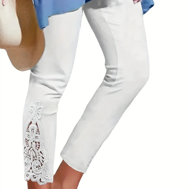 White capri pants with floral lace cutout detail on hem worn with blue top and carrying straw bag