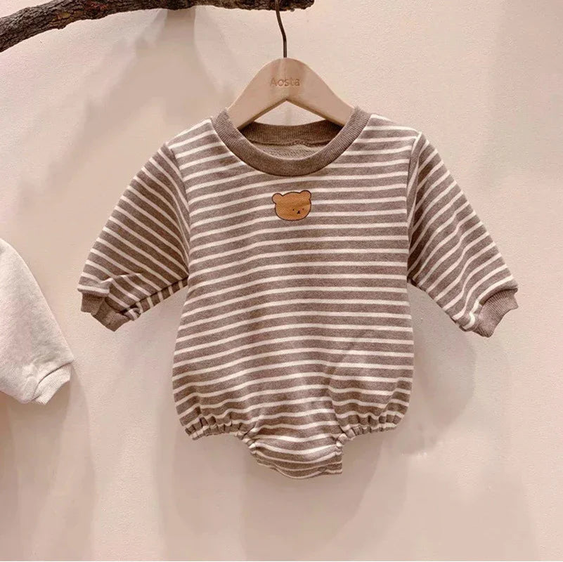 Brown and white striped baby romper with bear face patch on chest hanging on wooden hanger