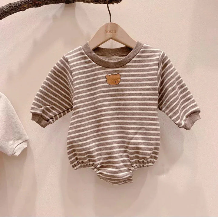 Brown and white striped baby romper with bear face patch on chest hanging on wooden hanger