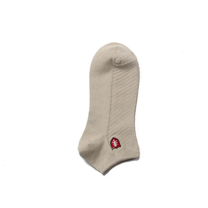Beige ankle sock with ribbed texture and small red leaf logo on white background