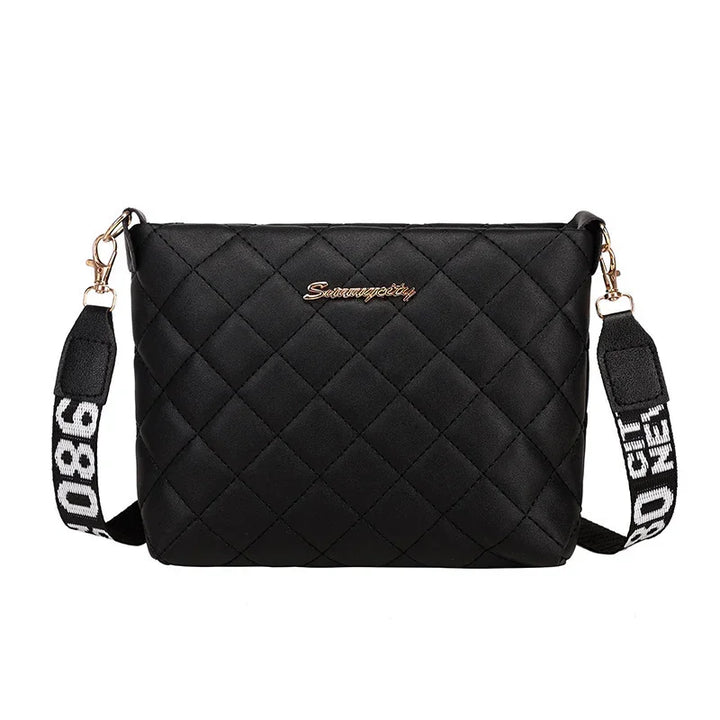 Black quilted crossbody bag with gold hardware and adjustable strap featuring white text
