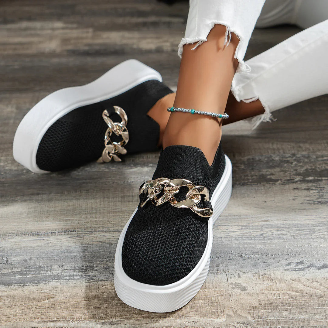 Black slip-on sneakers with chunky gold chain detail worn with white distressed jeans and beaded anklet