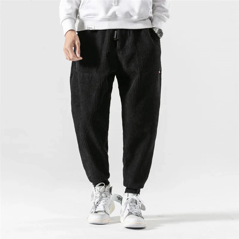 Man wearing black corduroy joggers with elastic cuffs and white high-top sneakers on white background
