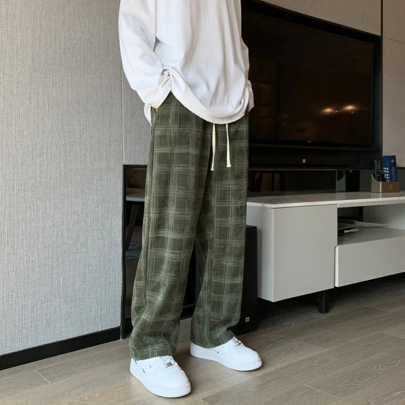 Man wearing olive green plaid pants with white drawstring and white sneakers in modern living room