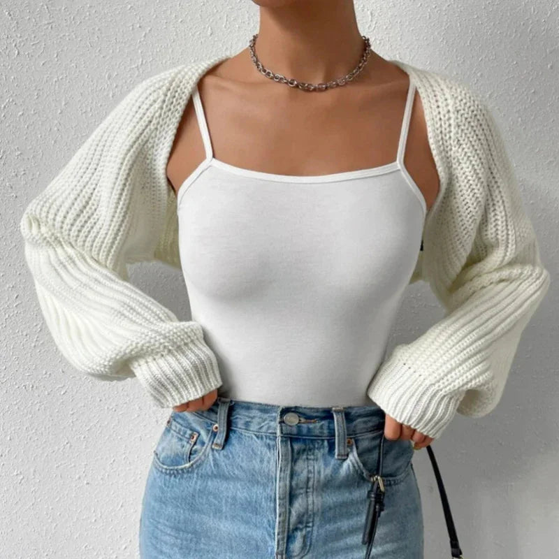 Woman wearing white knit shrug over white spaghetti strap top with high-waisted blue jeans