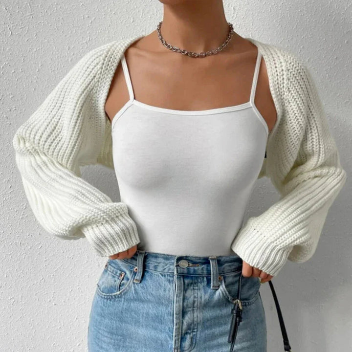 Woman wearing white knit shrug over white spaghetti strap top with high-waisted blue jeans