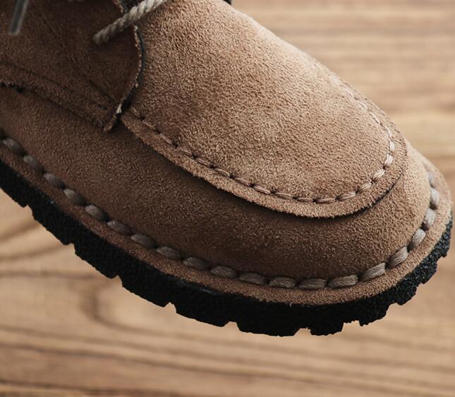 Close-up of a brown suede moccasin loafer with detailed stitching and black rubber sole on wooden surface