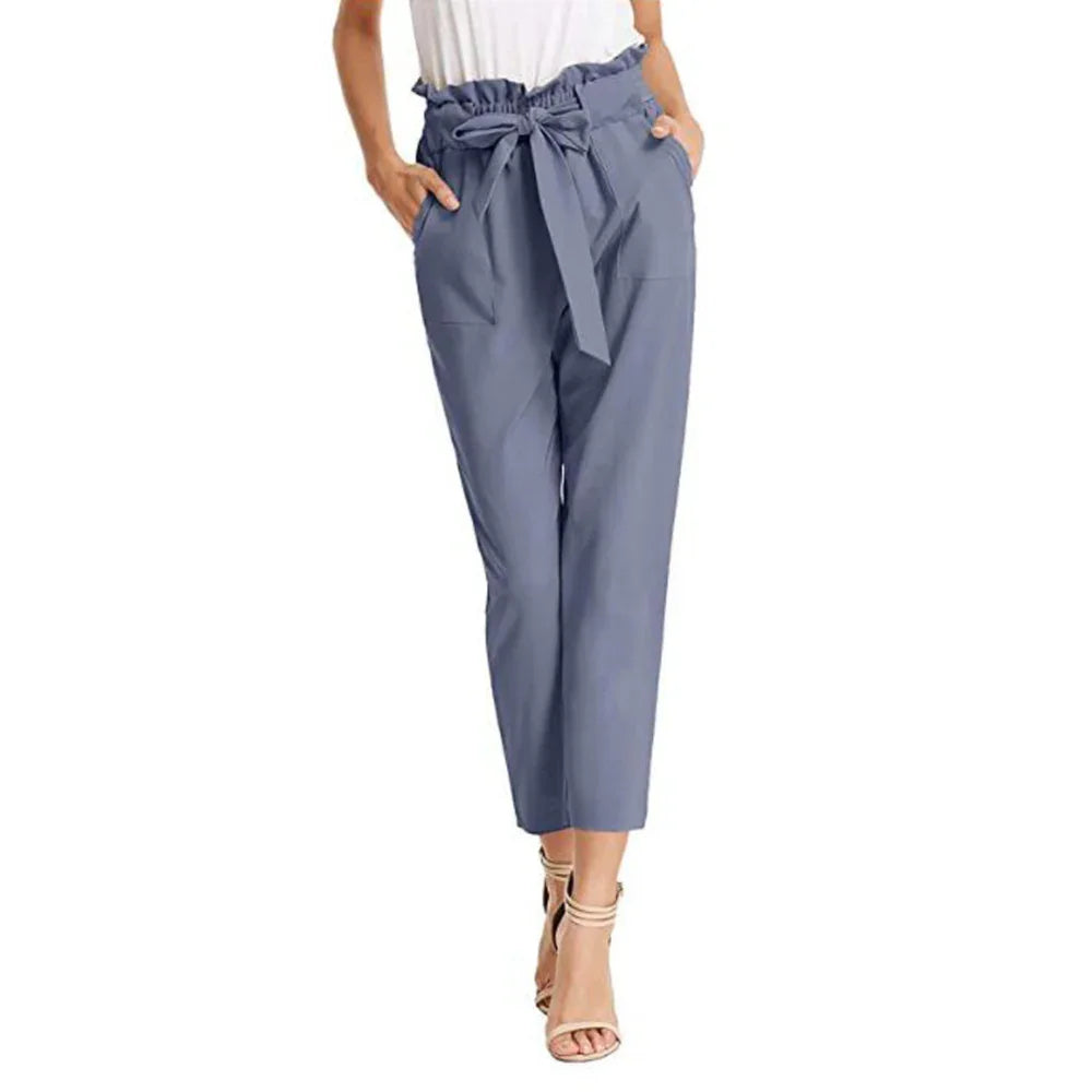 Woman wearing blue high waist paperbag pants with a tied belt and pockets, paired with nude heels