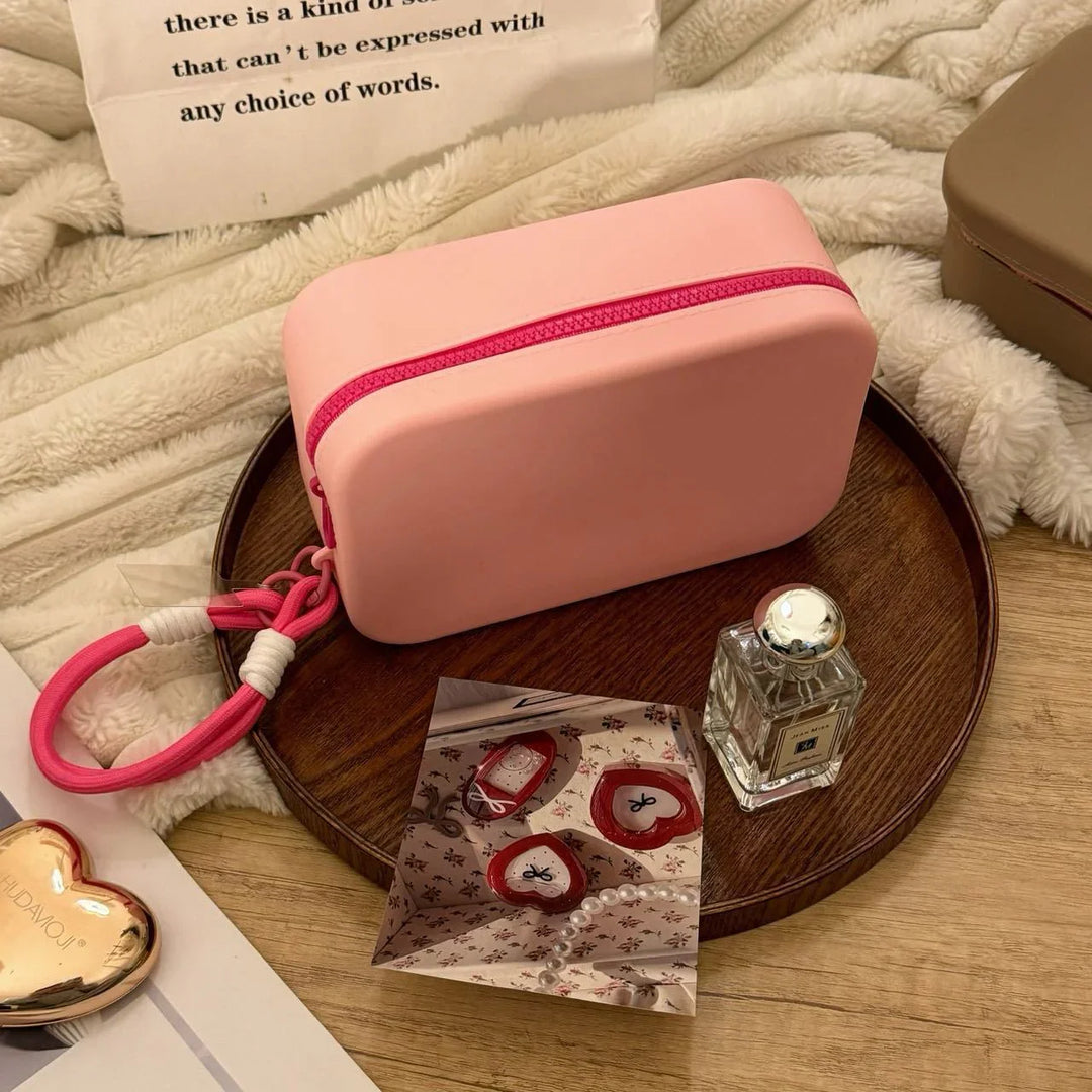 Pink rectangular pouch with zipper on wooden tray with perfume bottle and reflective card on cozy beige fabric
