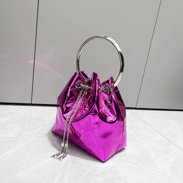 Shiny metallic fuchsia handbag with silver ring handle and chain tassels on marble floor