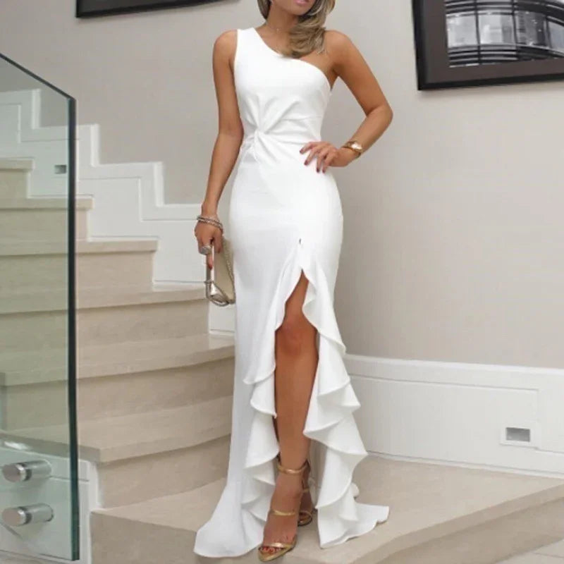 Woman in elegant white asymmetrical ruffle slit dress with gold heels standing on staircase