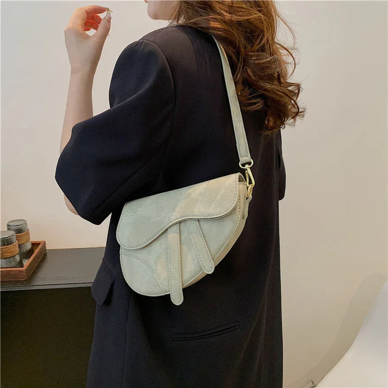 Woman wearing black blazer carrying beige leather saddle crossbody bag indoors