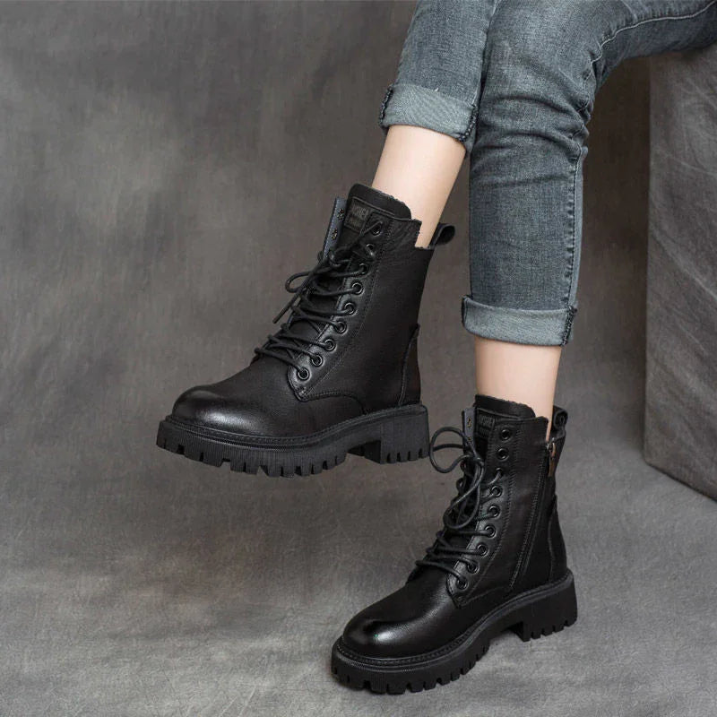 Black leather lace-up combat boots worn with rolled-up gray jeans on gray background