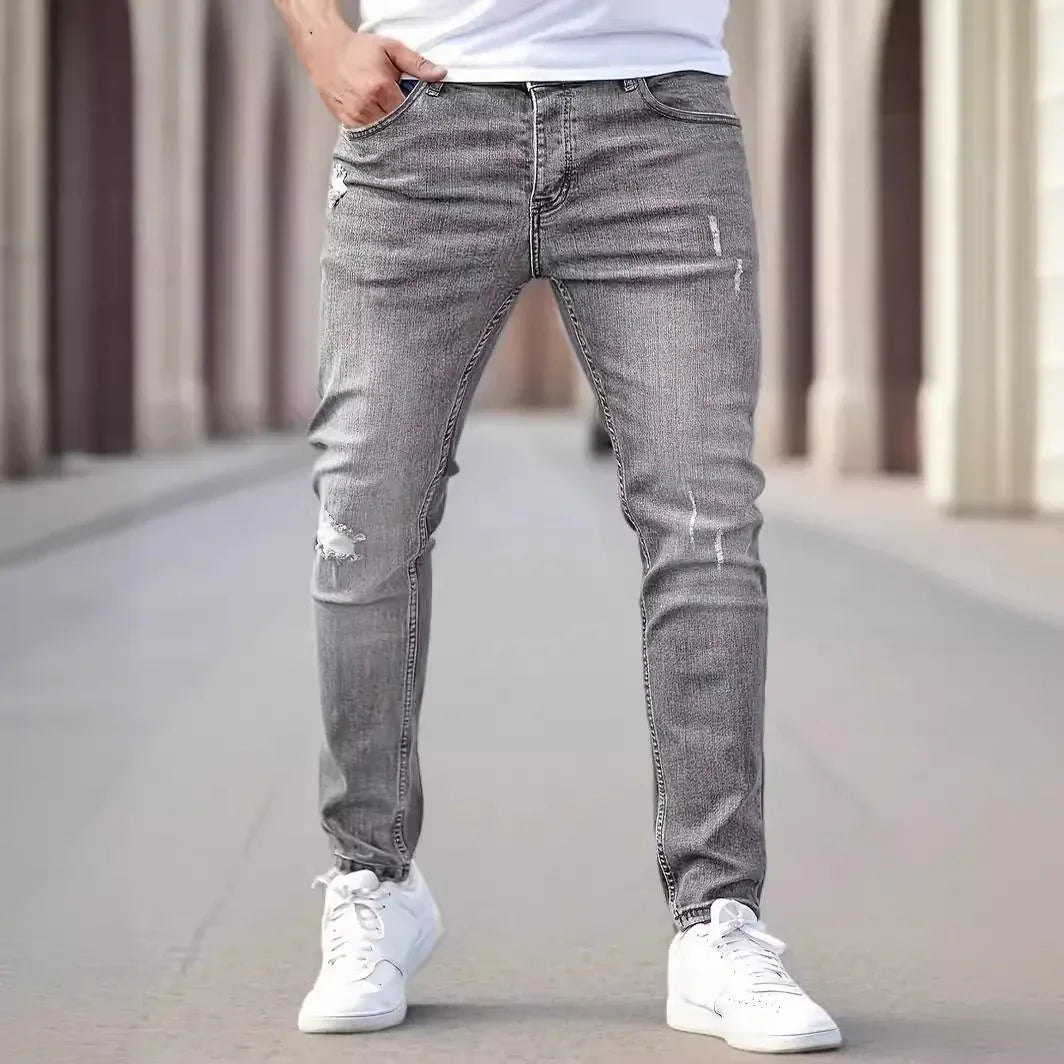 Man wearing distressed grey slim-fit jeans with white sneakers in urban setting