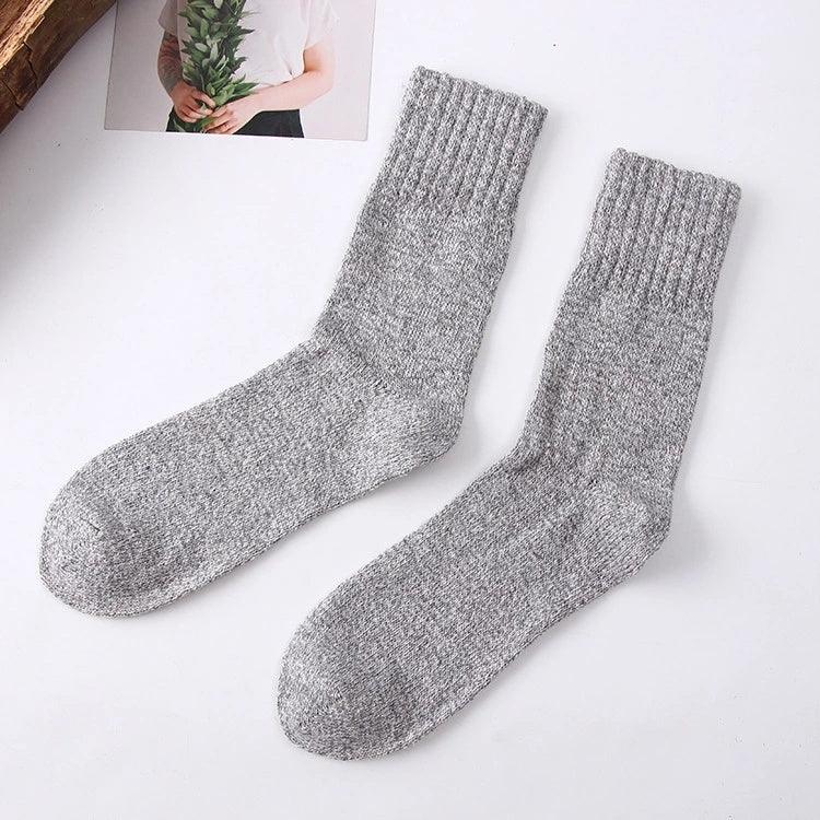 Pair of cozy grey knitted wool socks on white surface with a photo of person holding green leaves