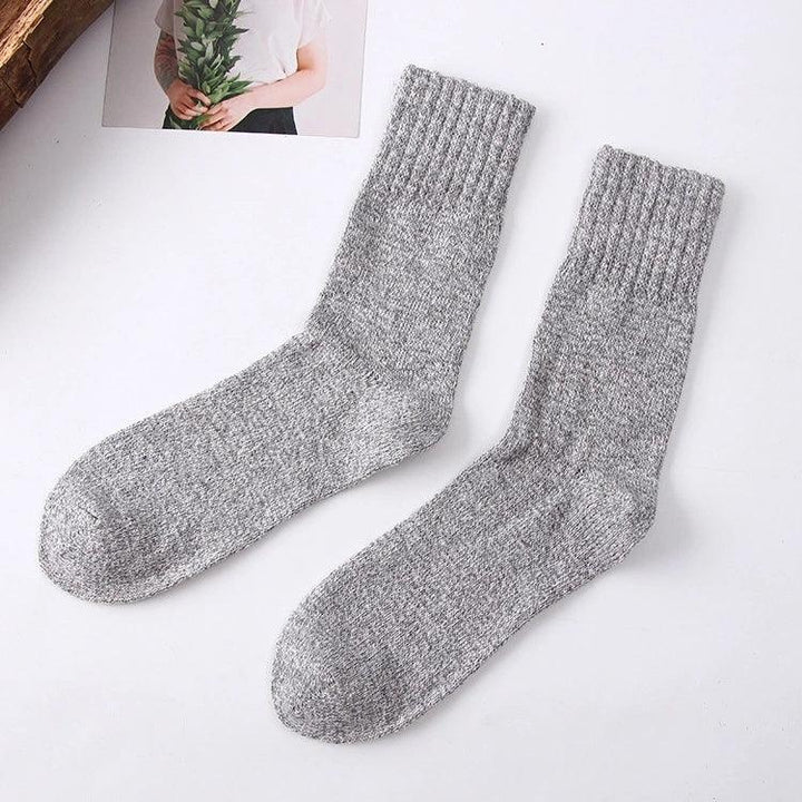 Pair of cozy grey knitted wool socks on white surface with a photo of person holding green leaves