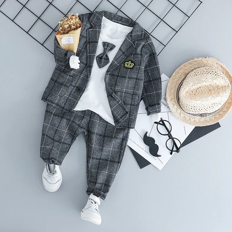 Toddler boy's gray plaid suit with white shirt and bow tie, white sneakers, straw hat, sunglasses on gray background