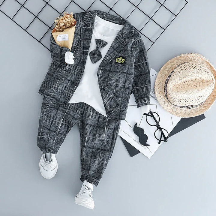 Toddler boy's gray plaid suit with white shirt and bow tie, white sneakers, straw hat, sunglasses on gray background