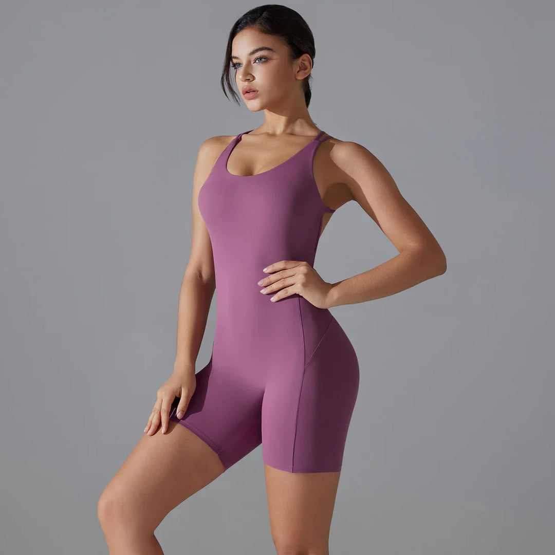 Woman wearing purple sleeveless fitness bodysuit posing against gray background