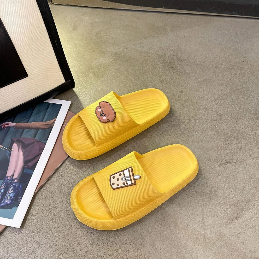 Pair of yellow slide sandals with cute brown dog and bubble tea designs on straps on gray floor
