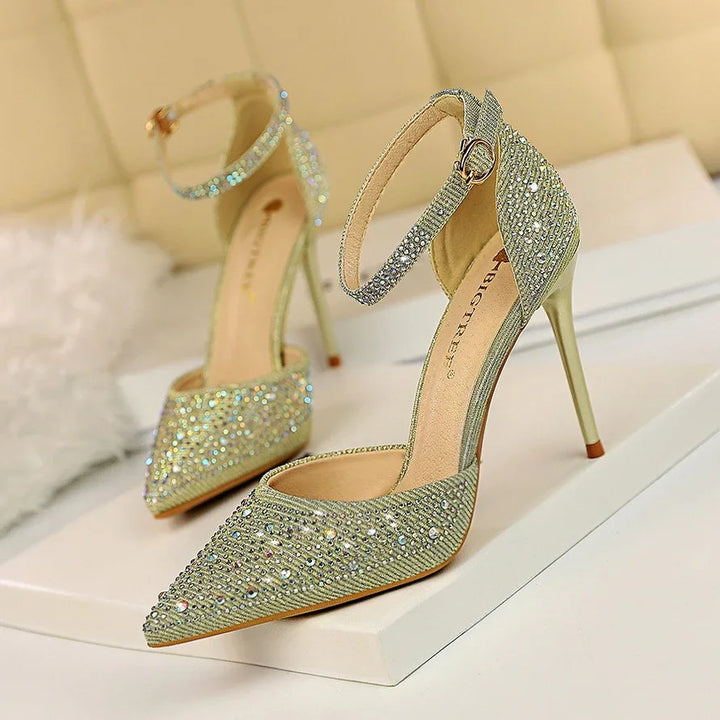 Elegant gold high heel shoes with ankle straps and rhinestone embellishments on white surface