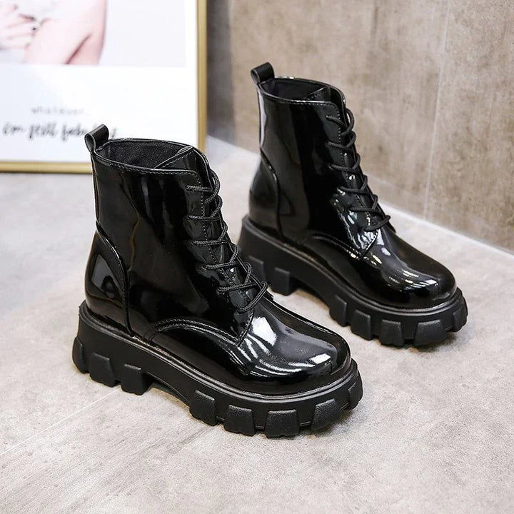 Pair of glossy black patent leather combat boots with chunky lug soles on gray floor