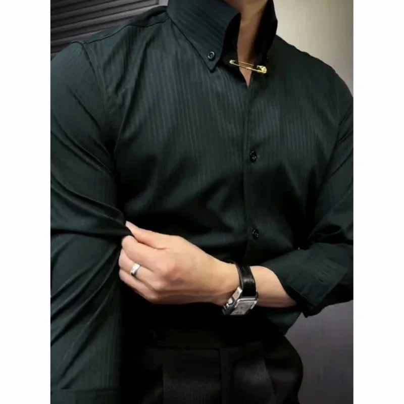 Man wearing dark green striped dress shirt with gold collar pin, adjusting sleeve, wearing silver watch and ring