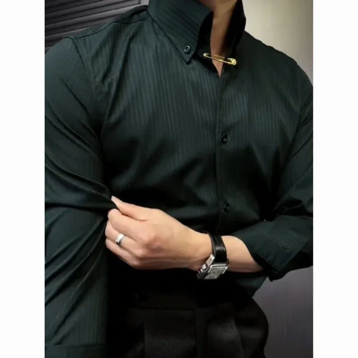 Man wearing dark green striped dress shirt with gold collar pin, adjusting sleeve, wearing silver watch and ring