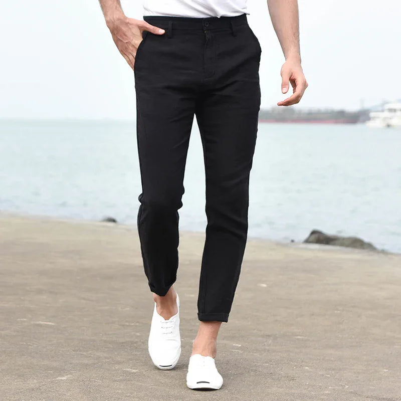 Man wearing slim-fit black pants and white casual shoes walking on waterfront promenade