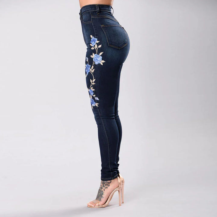 Side view of woman wearing dark blue skinny jeans with blue floral embroidery and beige high heels