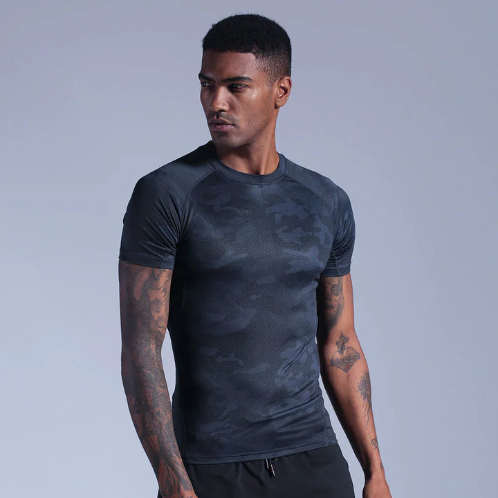 Man wearing fitted black camo athletic t-shirt with tattoos on arms against gray background
