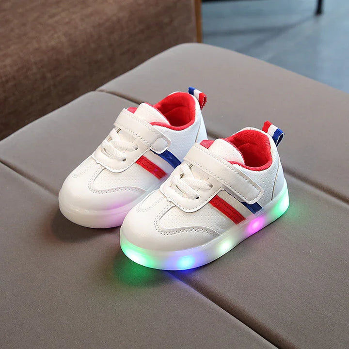 White kids sneakers with red and blue stripes, light-up colorful LED soles, and Velcro straps on gray cushion