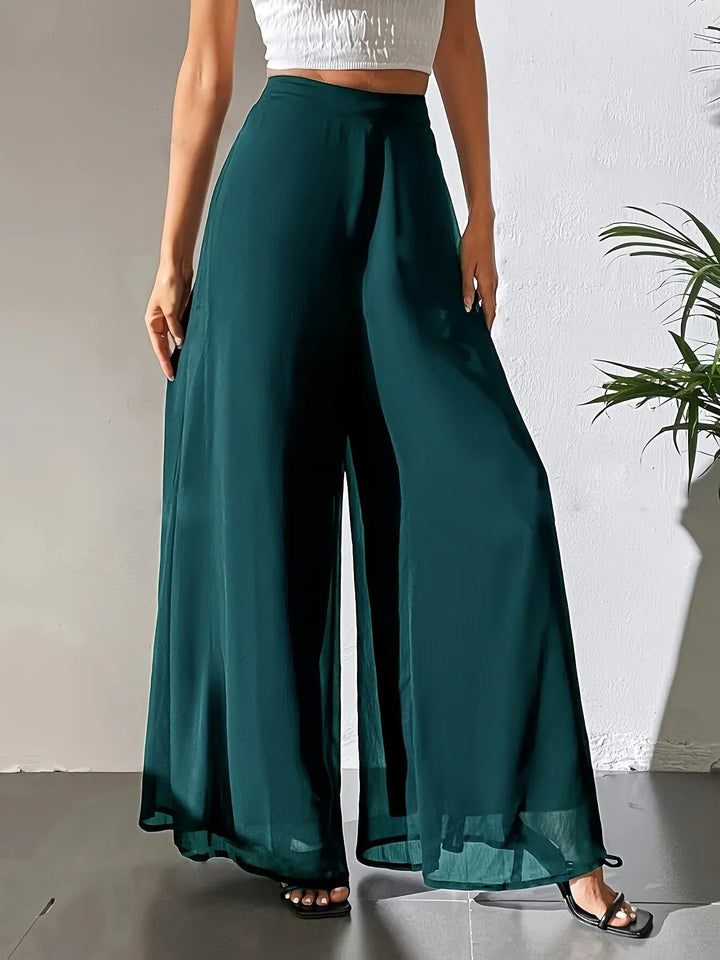 Woman wearing dark green wide-leg chiffon pants and white cropped top in minimalist indoor setting
