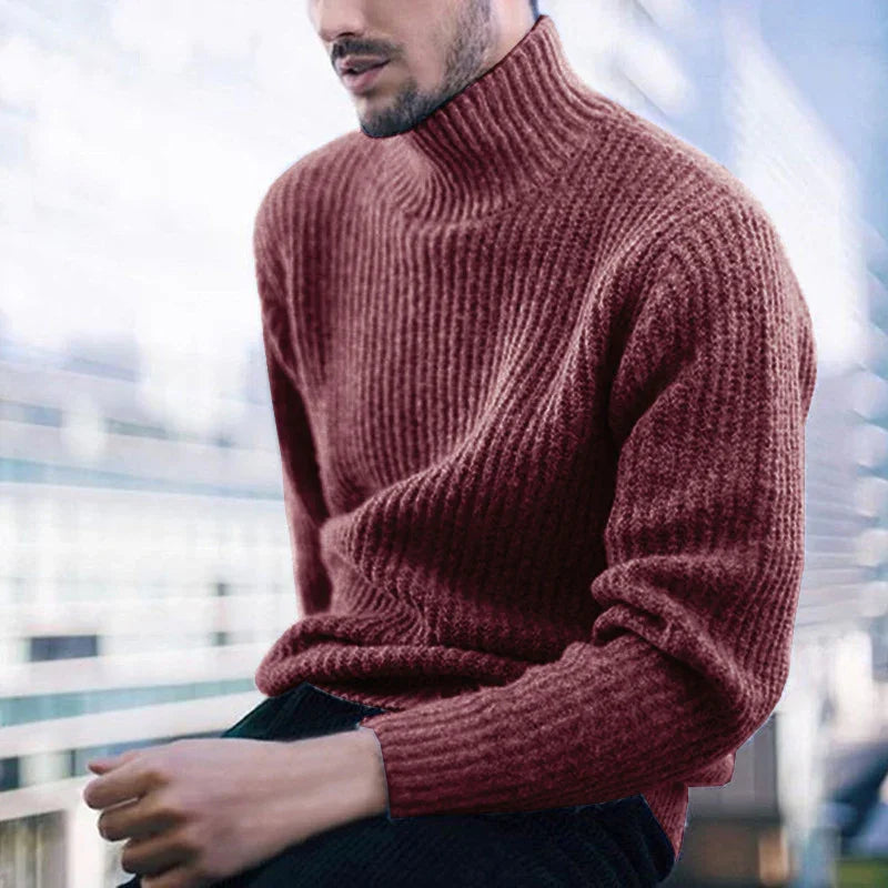Man wearing a cozy brown ribbed turtleneck sweater sitting by a window with blurred city background