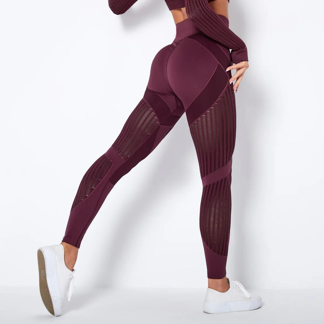 Woman wearing high-waisted burgundy leggings with mesh panels and white sneakers against white background