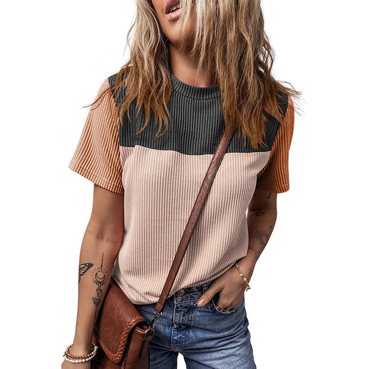 Woman wearing a color-blocked ribbed short-sleeve top with black, beige, and orange sections, paired with blue denim jeans and a brown leather crossbody bag