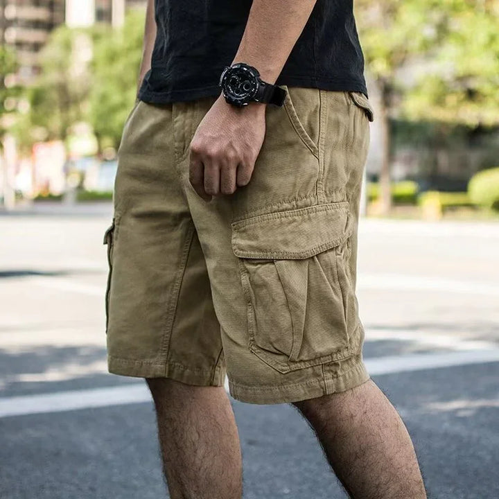 Man wearing khaki cargo shorts and black watch standing outdoors on urban street