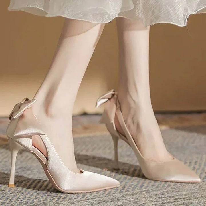 Elegant beige satin high heels with side cutouts and decorative bows, worn with a sheer skirt
