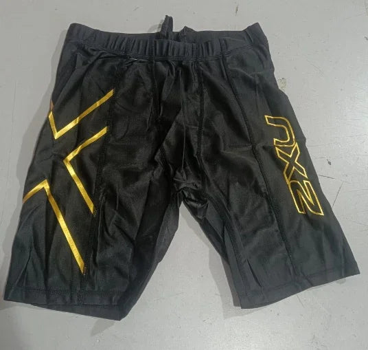 Black 2XU compression shorts with gold logo and lines on a light gray surface