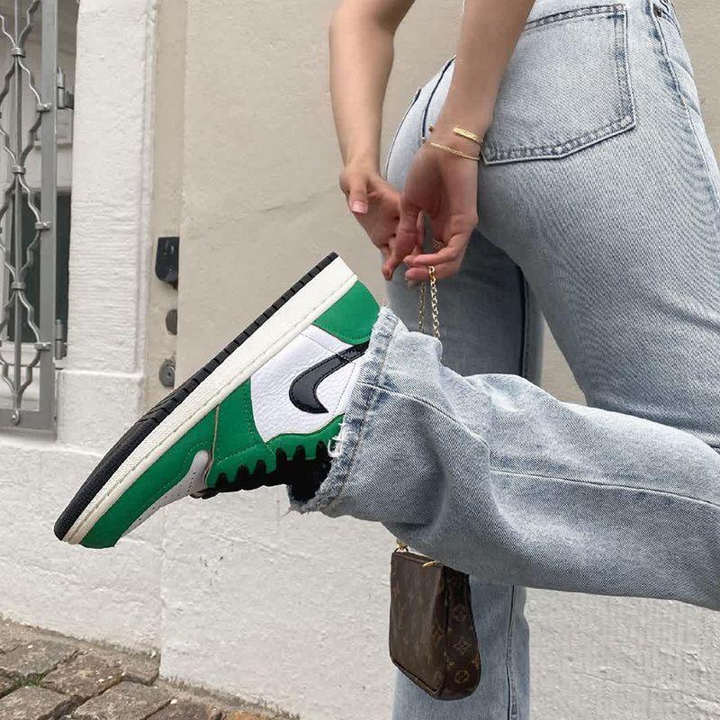 Person wearing light blue jeans and green white black Nike sneakers, holding brown designer purse outside