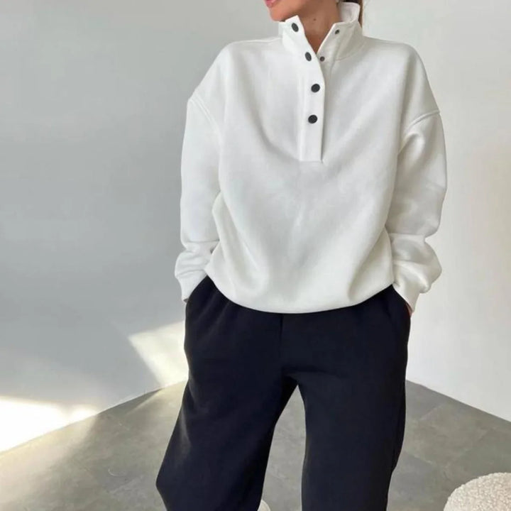 Woman wearing a white button-up high collar sweatshirt and black pants in a minimal indoor setting