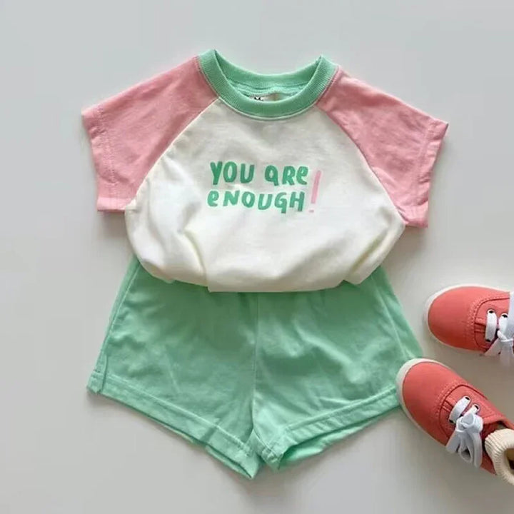 Children's casual outfit with pink sleeves, green trim shirt reading 'You Are Enough', green shorts, and coral shoes