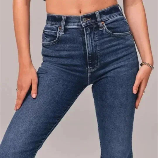 Close-up of high-waisted dark blue denim jeans worn by a person with hands resting on thighs