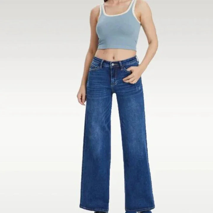 Woman wearing light blue crop top and high-waist wide leg blue jeans on white background