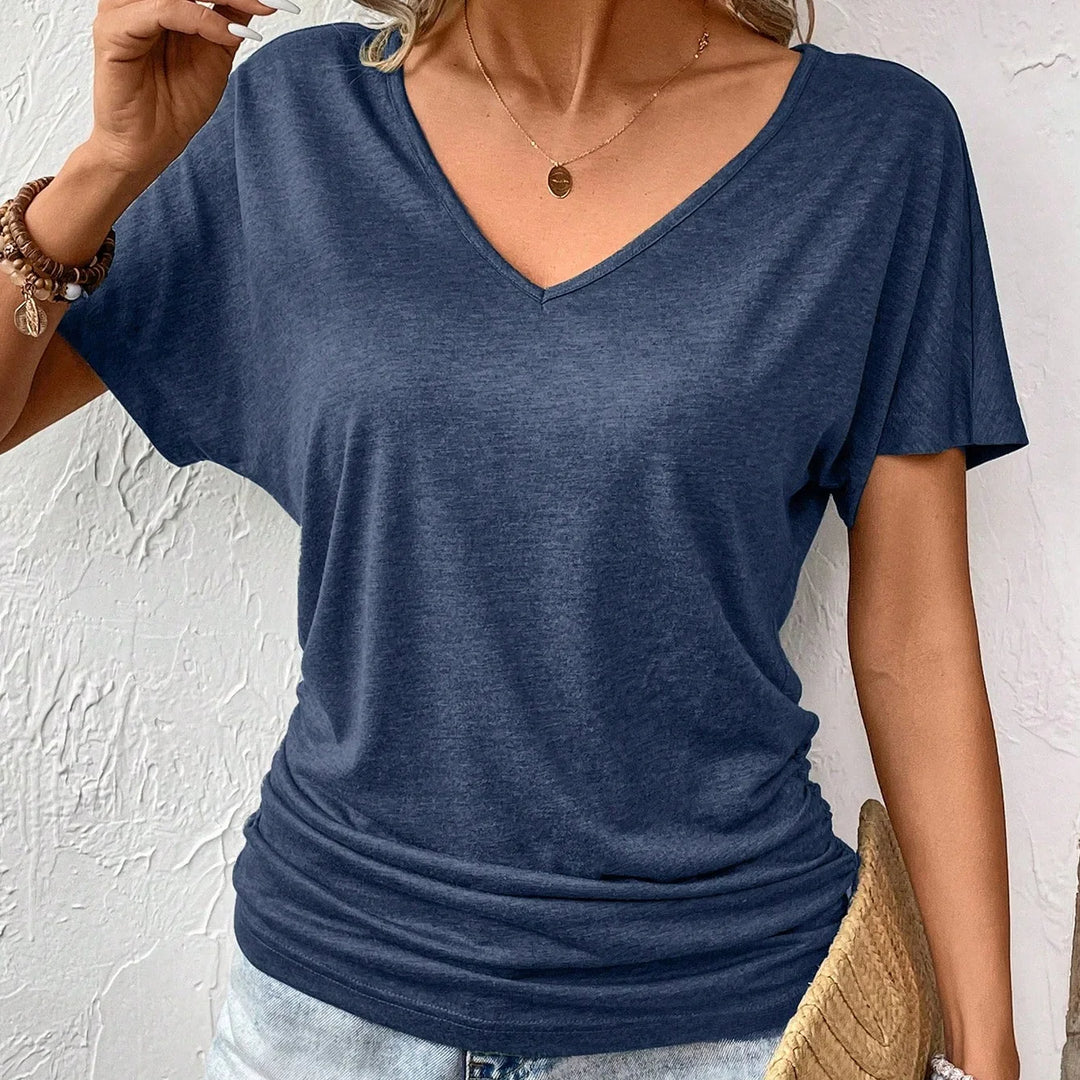 Woman wearing navy blue V-neck casual T-shirt with ruched sides and bracelets, holding straw clutch