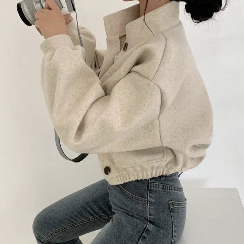 Woman in beige cropped wool jacket and blue jeans holding a camera on white background