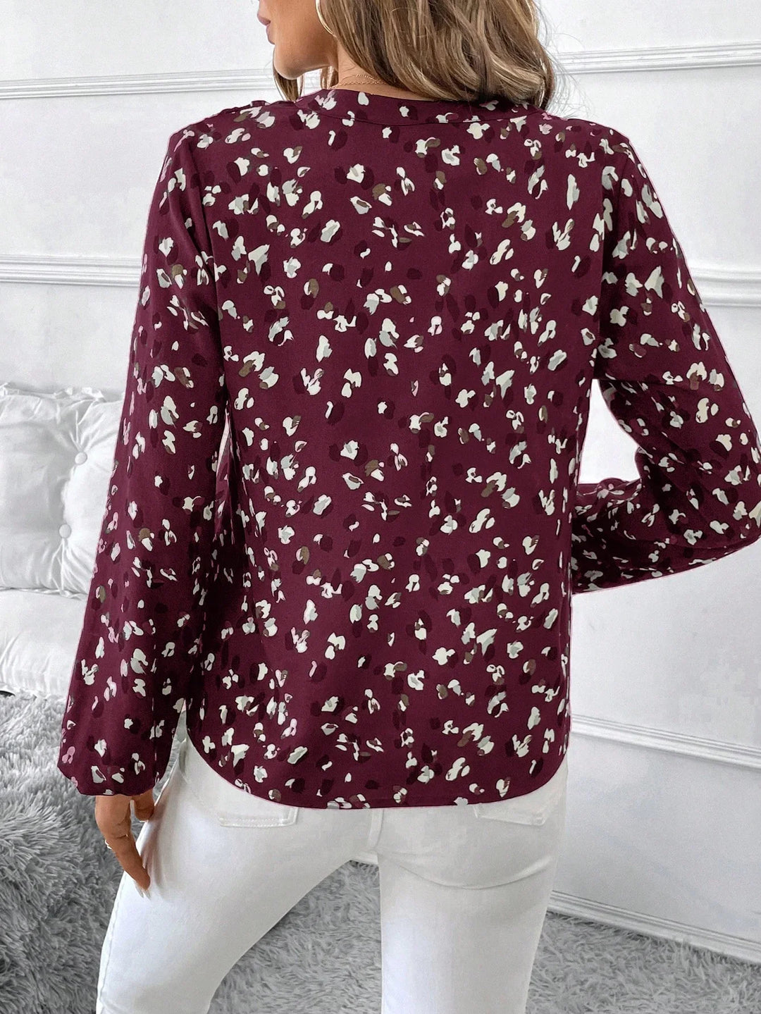 Woman wearing maroon long-sleeve blouse with white and brown floral print, paired with white pants